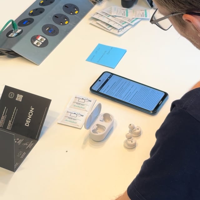 A participant reading the setup instructions on screen, earbuds and open case on the table.